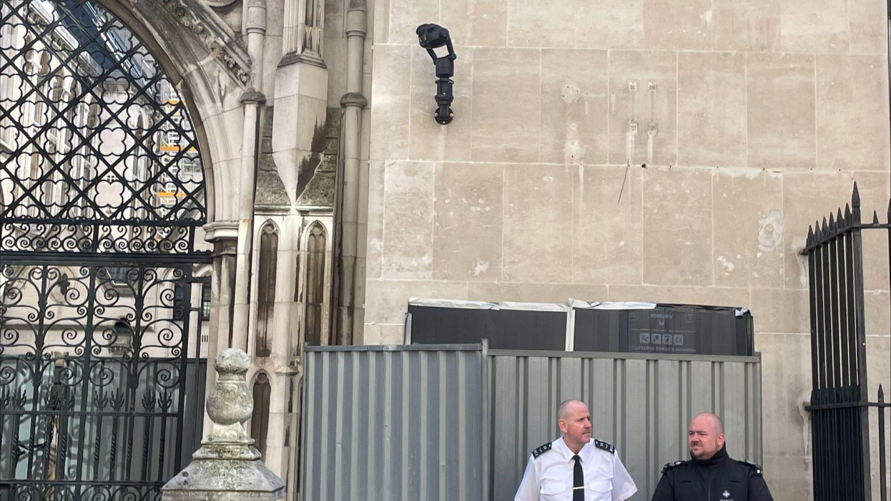 Dvojica članova obezbeđenja stoje ispred metalnih barijera iza kojih je Benksijev mural 