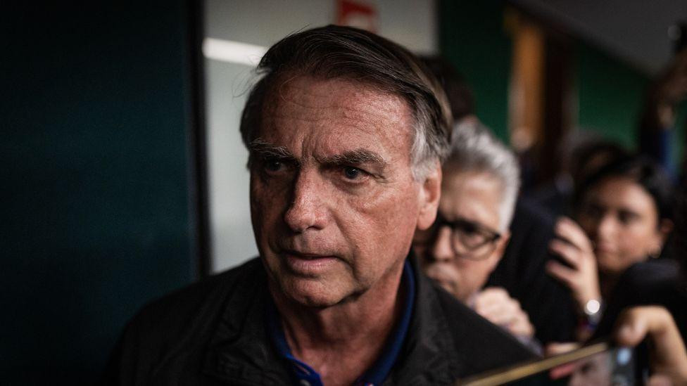 Žair Bolsonaro u tamno plavoj majici i crnoj jakni gleda u daljinu 