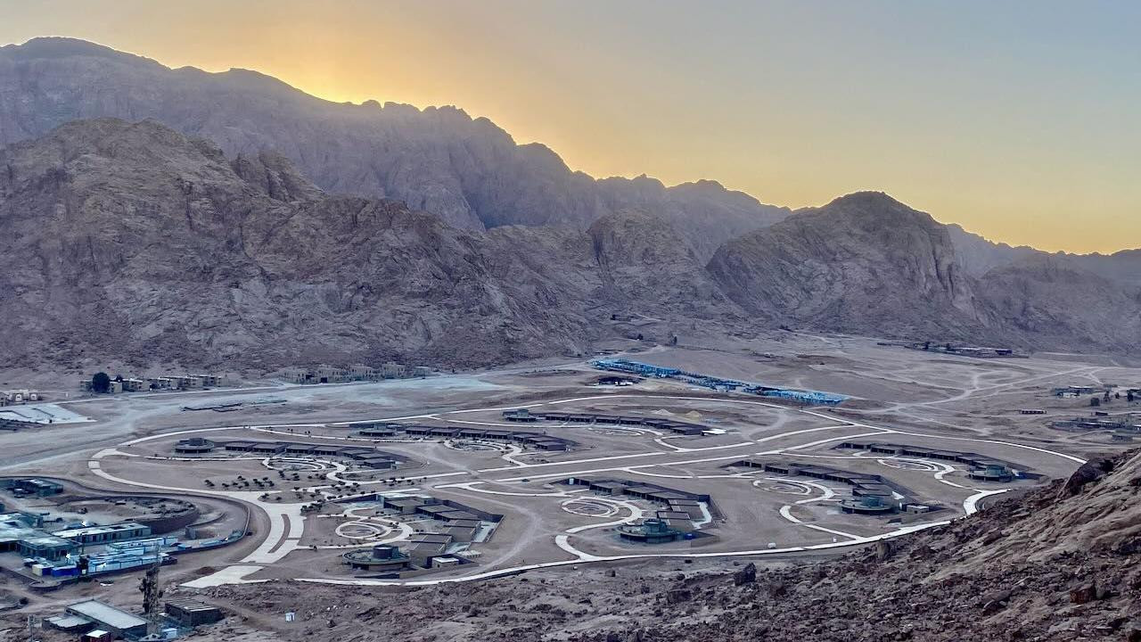 Pogled na jedan od objekata, koji je još u izgradnji, ravnica el-Raha. Sunce je iza okolnih planina, dok je gradilište u prvom planu, sa putevima koji povezuju različite zgrade.