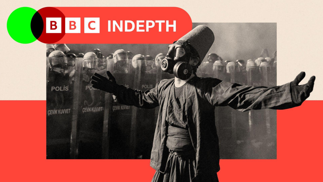 A protester wearing a whirling dervish costume performs in front of Turkish riot police barricades