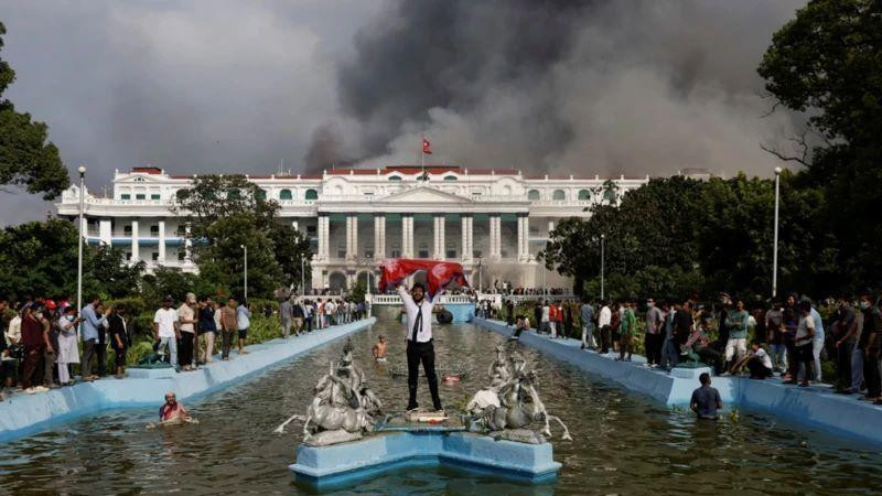 Muškarac slavi držeći zastavu Nepala ispred zgrade parlamenta iz koje izbija dim