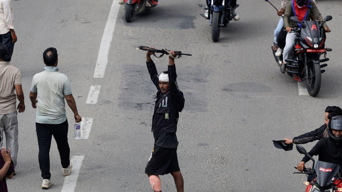 Muškarac sa zavojem na glavi na ulici drži pušku visoko podignutu u vazduh