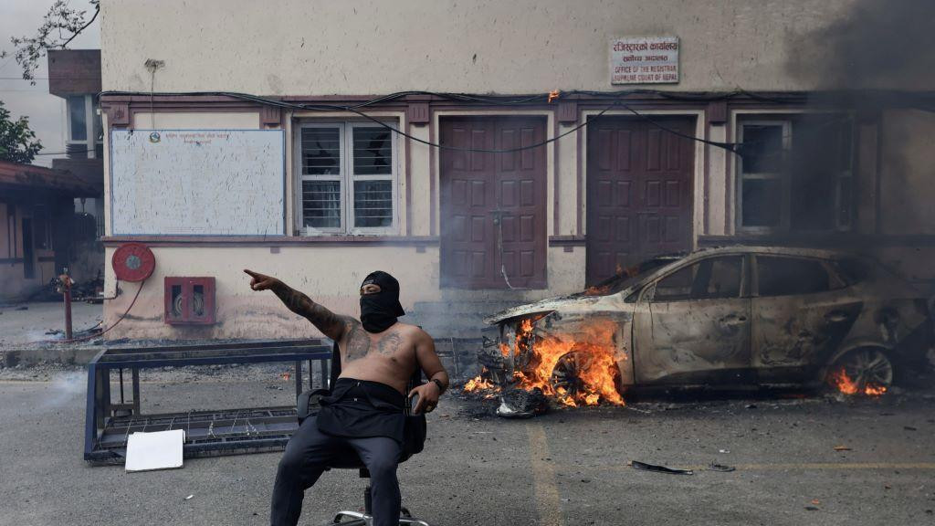 Demonstrant sa maskom preko lica i bez majice sedi ispred auta koji gori