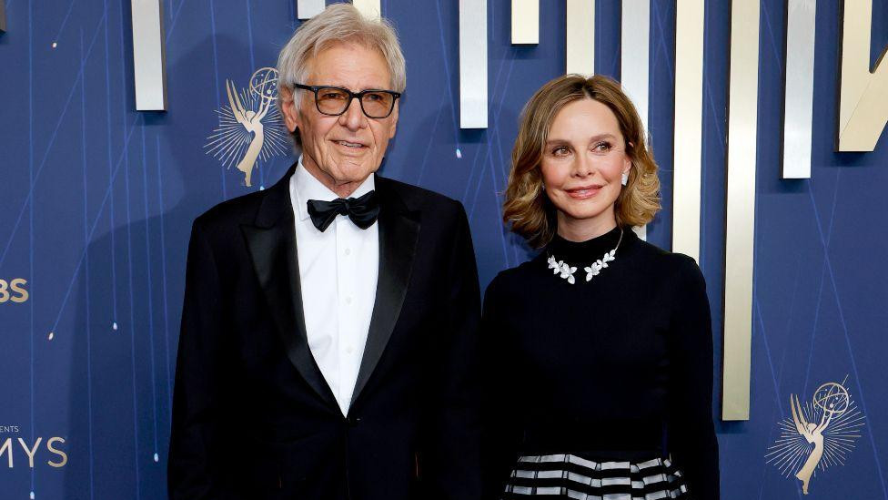 Harrison Ford u crnom odelu I beloj košulji sa suprugom Kalistom Flokhart u crnoj košulji i dugačkoj crno sivoj suknji