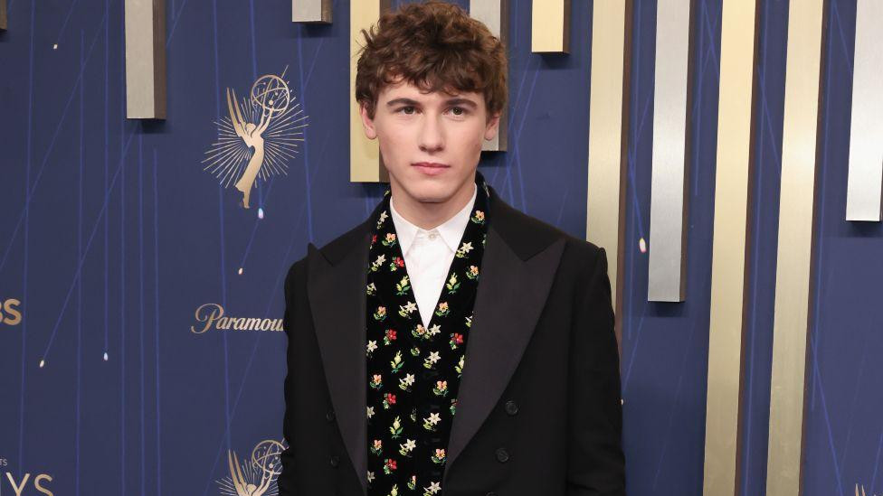 Glum Sem Nivola u beloj košulji, šarenom prsluku i crnom sakou