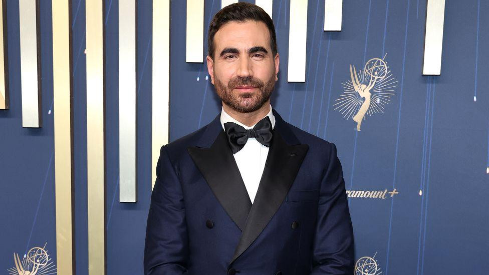 Glum Bret Goldstein u crnom odelu, beloj košulji sa crnom leptir mašnom