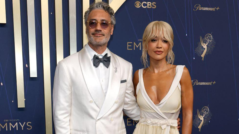 Reditelj Taika Vaititi u belom odelu sa suprugom pevačicom Ritom Orom u beloj haljini