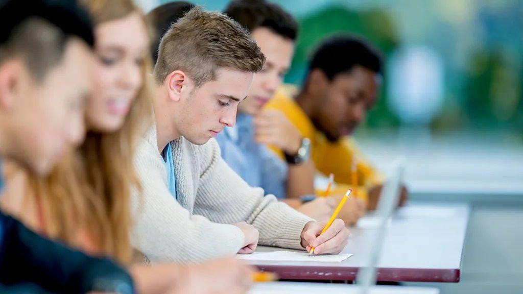 Muškarac piše rukom za stolom među drugim ljudima