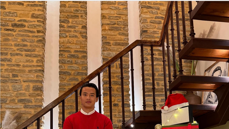 Saugat Tapa, u crvenom džemperu i crnim pantalonama, pored božićne jelke napravljene od kutija luksuznih brendova 