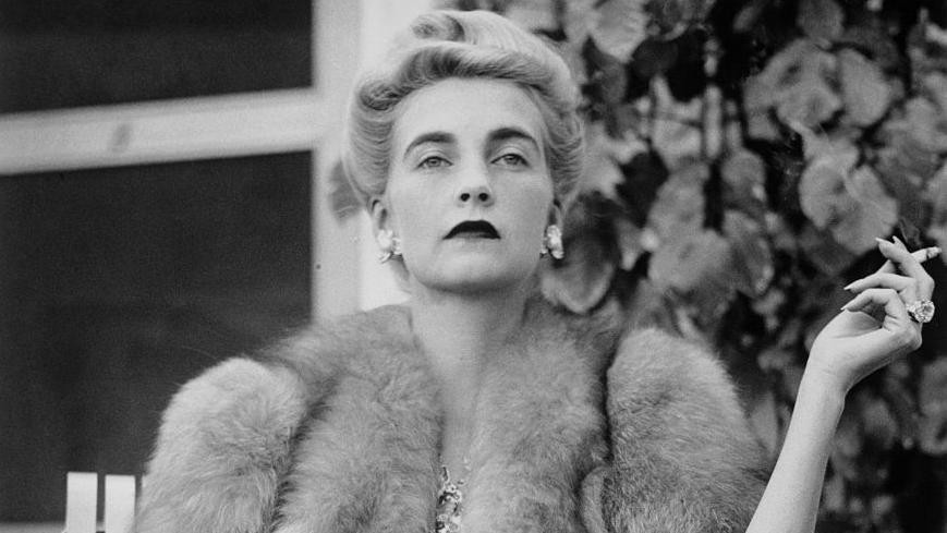 Crno-bela fotografija žena koja u jednoj ruci drži cigaretu dok joj je pas u krilu 