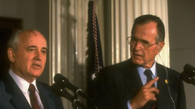 Dvojica muškaraca u odelima stoje za govornicom 