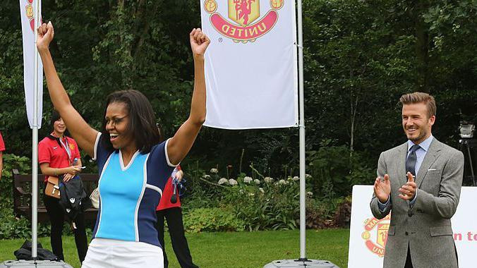 Mišel Obama podiže ruke u vazduh i navija, Dejvid Bekam stoji iza nje 