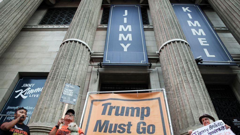 Tri žene ispred zgrade u kojoj se snima šou Džimija Kimela a između njih je transparent na kome piše "Tramp mora da ode"