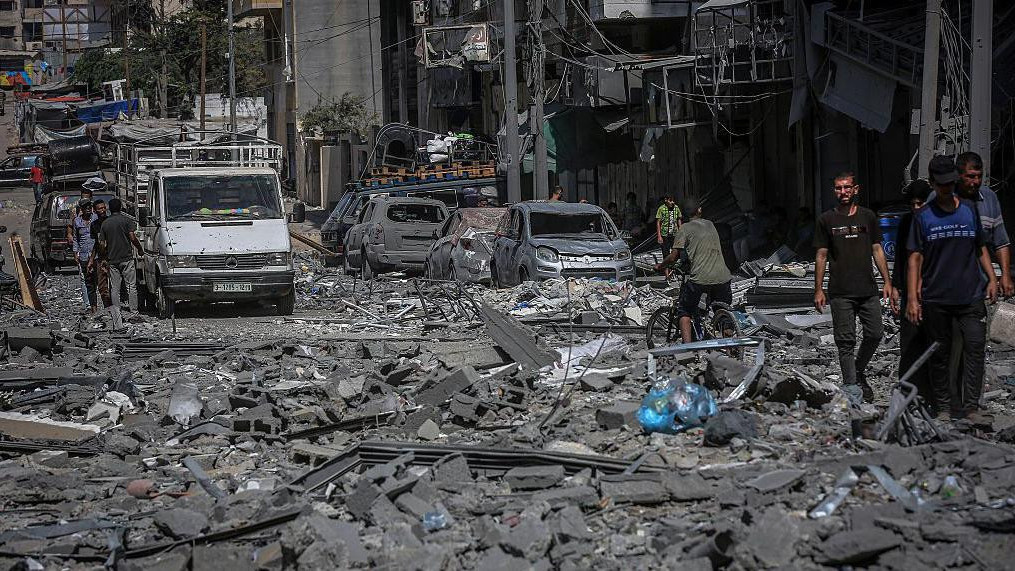 Ulica u naselju Rimal u gradu Gazi je prekrivena ruševinama. Mnogo uništenih automobila može se videti duž ulica dok se ljudi okupljaju u malim grupama.