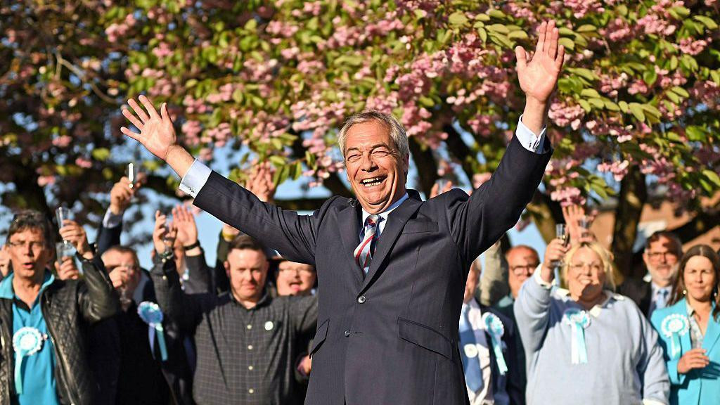 Najdžel Faraž se smeje sa podignutim rukama dok su iza njega ljudi koji ga podržavaju sa takođe podignutim rukama 