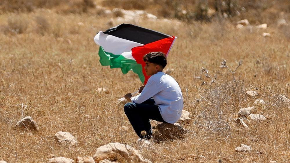 
                    A boy holds a Palestinian flag during a demonstration against what Palestinians say is Israel's confiscation of their land, as Isareli security forces stand guard, in Rab