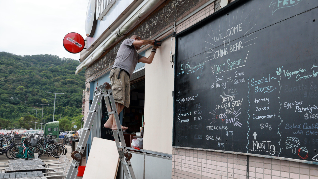 kina, tajfun ide ka kini, nevreme, muškarac zakucava drvene ploče kao zašzita od nevremena