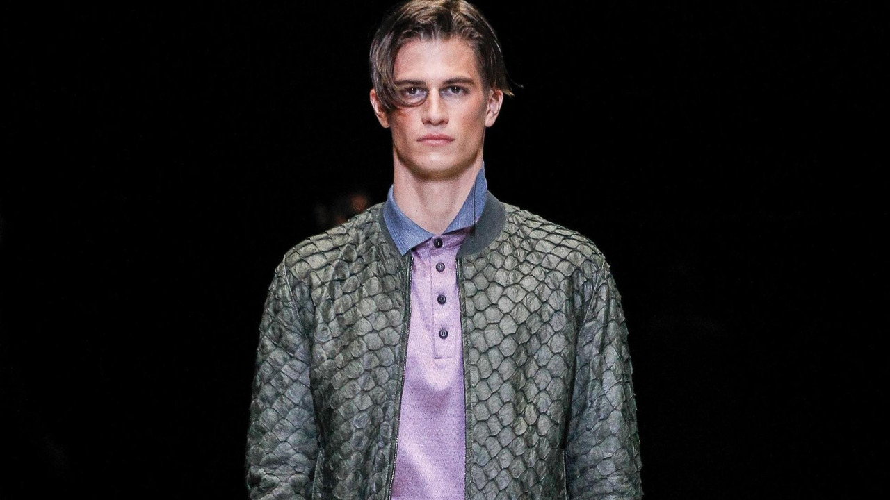 Muškarac, model u sivoj piraruku kožnoj jakni ispod koje je ljubičasto polo majica sa plavom kragnom