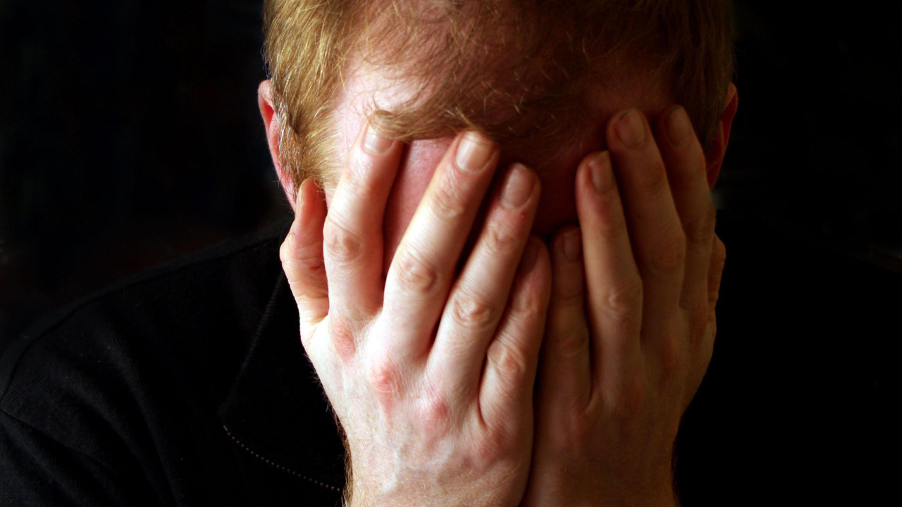 muškarac prekriva lice rukama, očajan muškarac