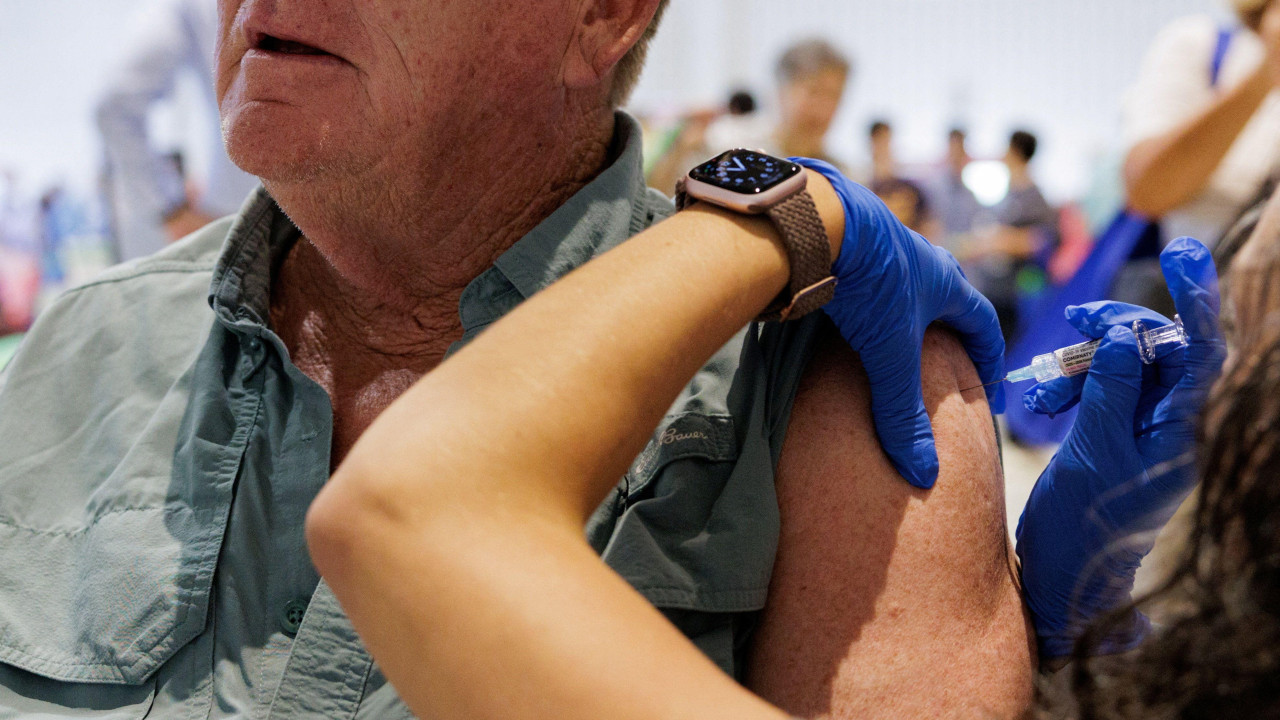 Muškarac sedi dok mu žena daje vakcinu u ruku