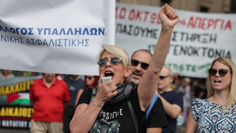 Jednodnevni štrajk radnika u Grčkoj zbog vladinog predloga da poslodavci mogu da produže radno vreme do 13 sati, žena u crnoj majici i plavom kosom drži uzdignutu pesnicu i govori u megafon