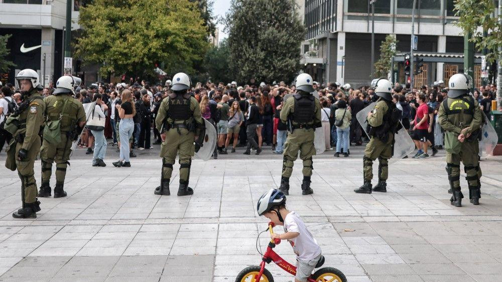 Dete vozi bicikl dok policija za suzbijanje demonstracija stoji na straži tokom demonstracija povodom 24-časovnog generalnog štrajka u Atini protiv reforme kojom se produžava 13-časovno radno vreme za radnike sa jednim poslom