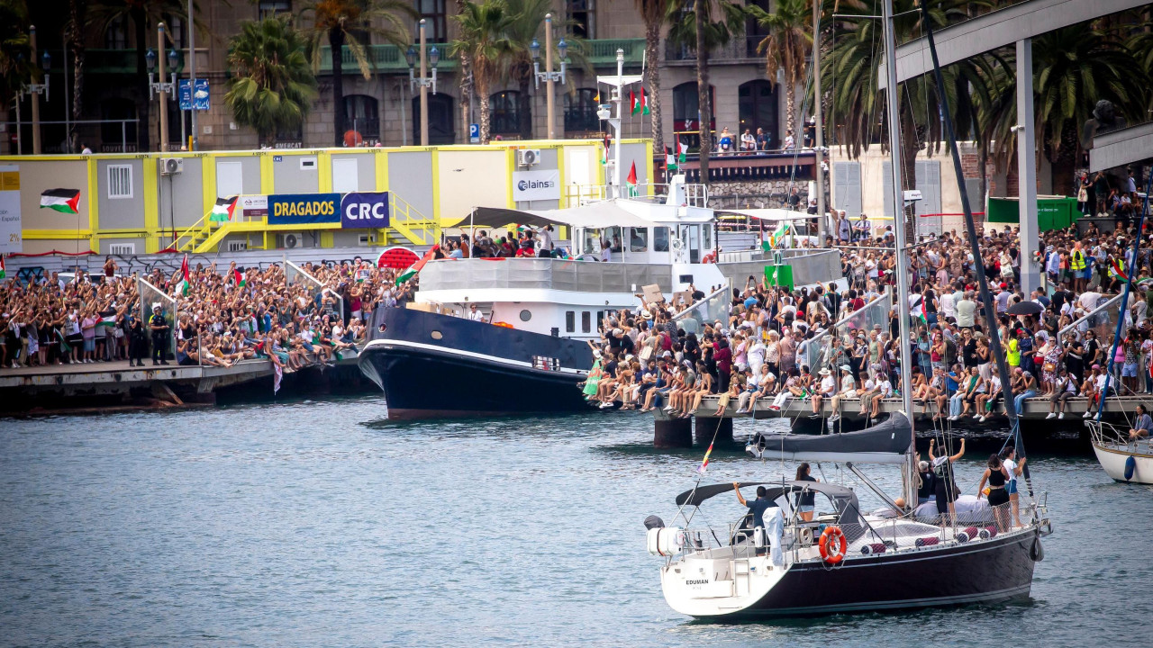 Stotine ljudi se okupilo u Barseloni kako bi se oprostilo od Globalne Sumud flotile. Mnoštvo pristalica koji nose kufije (palestinske marame) i mašu zastavama može se videti dok veliki čamac isplovljava, a u prvom planu se može videti i manja jedrilica.