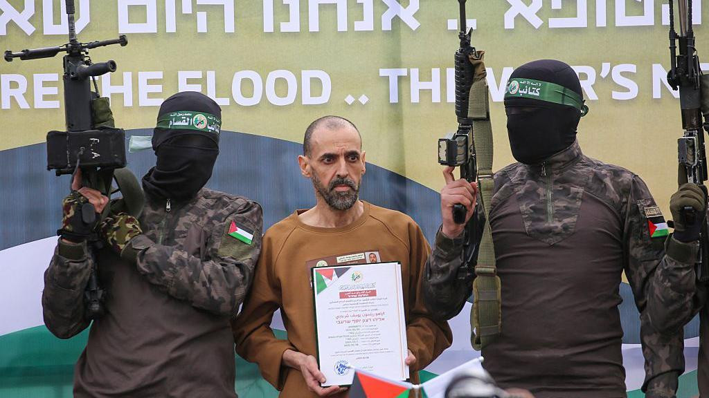 Naoružani borci Hamasa sa maskama na licima i izraelski taoc Elij Šarabi na bini