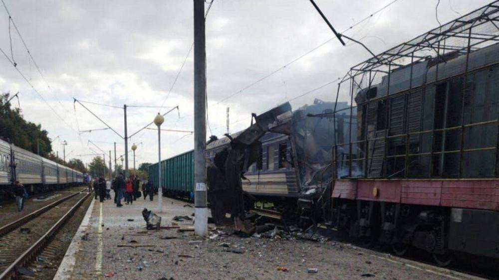 A train hit by a drone strike sits damaged at the railway station in Shostka. A group of people stands on the central platform in the distance.