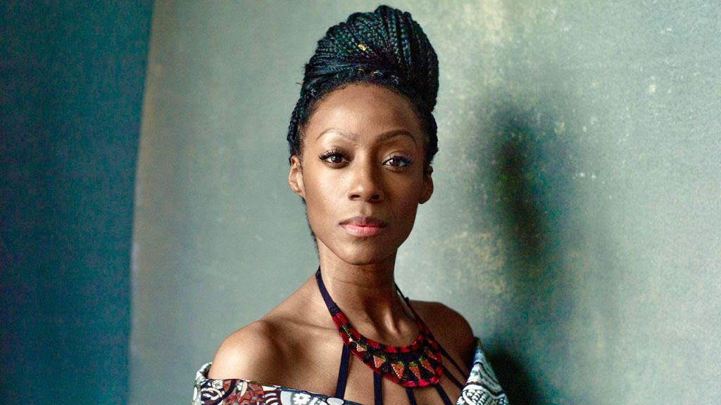 Portret Viktorije. Ima dugu pletenicu u punđi na vrhu glave. Nosi šarenu haljinu koja spušta ramena i veliku šarenu ogrlicu od perli koja je pričvršćena na vrhu brojnim crnim trakama.