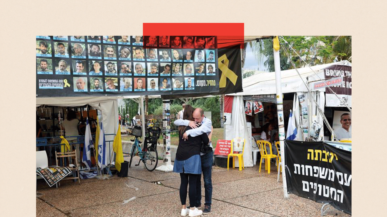 Muškarac i žena se grle ispred plakata sa fotografijama talaca