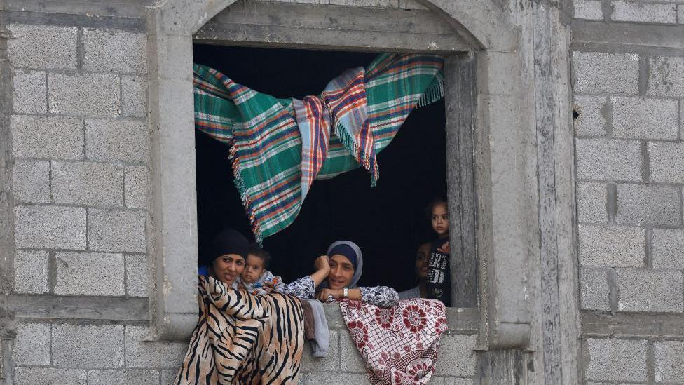 žene i deca gledaju kroz prozor kamene zgrade 