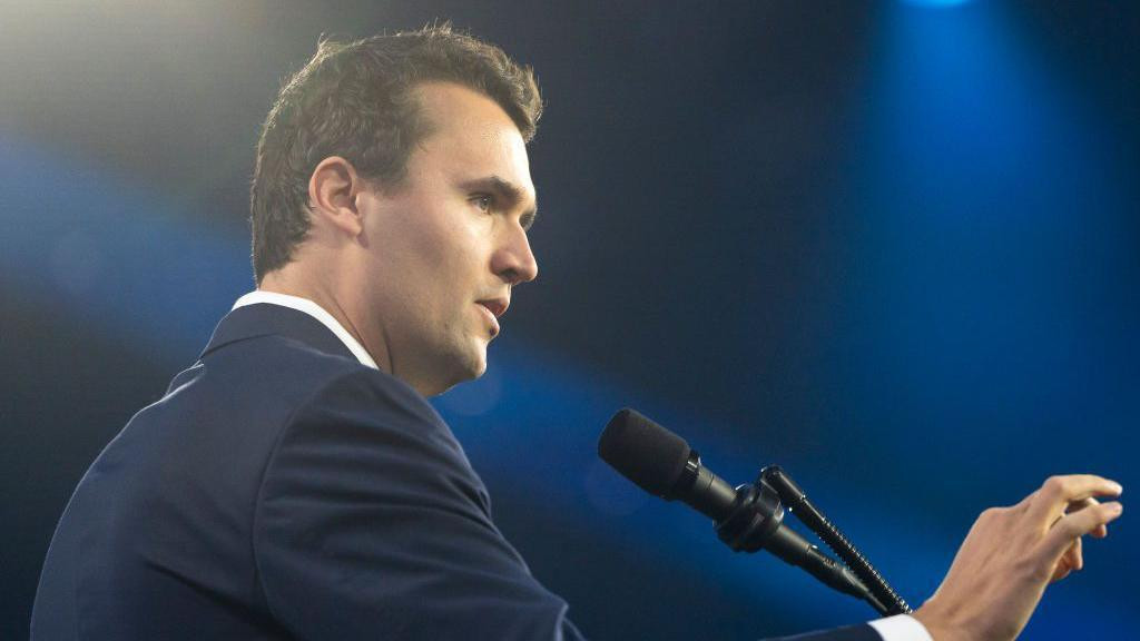Charlie Kirk is speaking behind a podium at a convention in Phoenix, Arizona