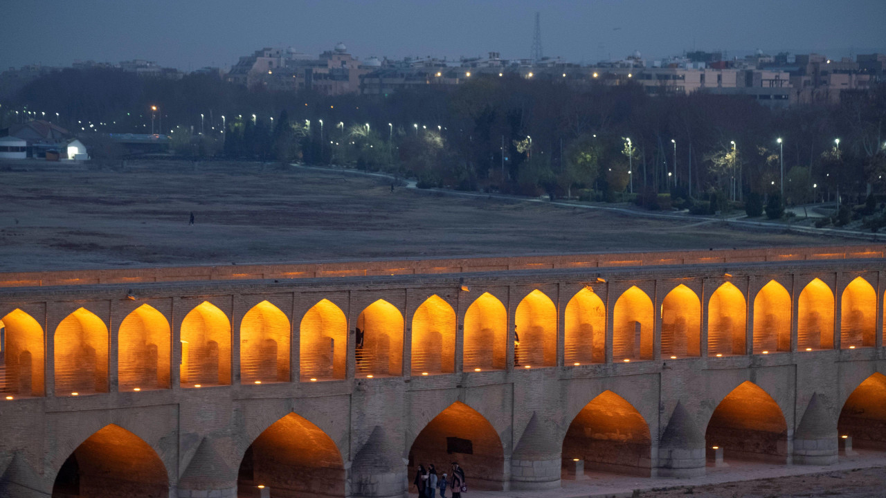 Osvetljen u sumrak, Isfahanski most sa 33 luka iz ranog 17. veka premošćuje osušeno korito reke Zajandeh Rud, dok ga grupa pešaka prelazi
