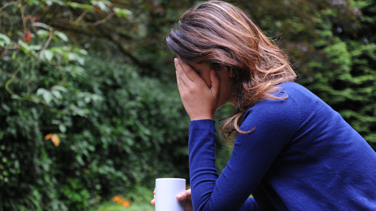 Zabrinuta žena se drži za glavu dok u ruci ima šolju 