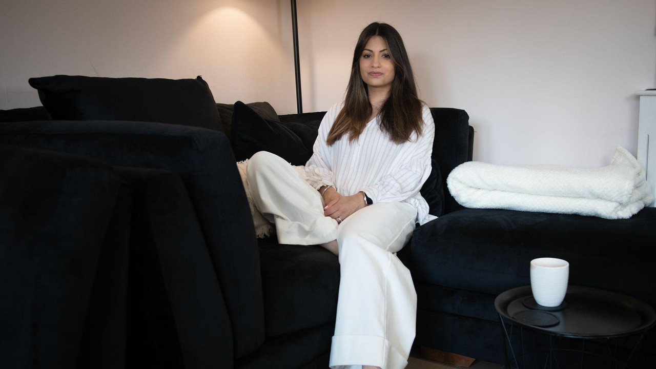 Džaslin nosi belu trenerku i sedi na cromo kauču. Pored nje je belo ćebe i bela šolja na crnom stočiću