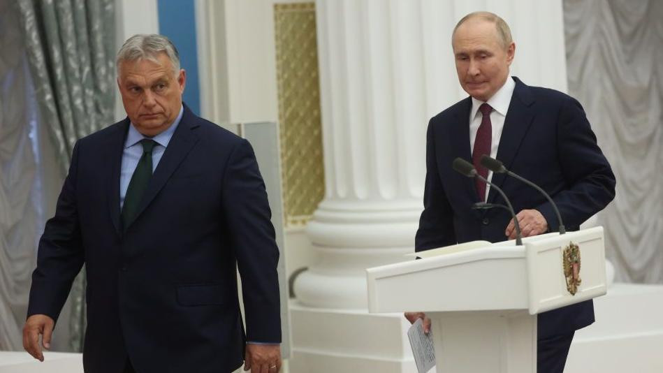 Dvojica muškaraca u odelima prolaze pored govornice, obojica deluju zabrinuto