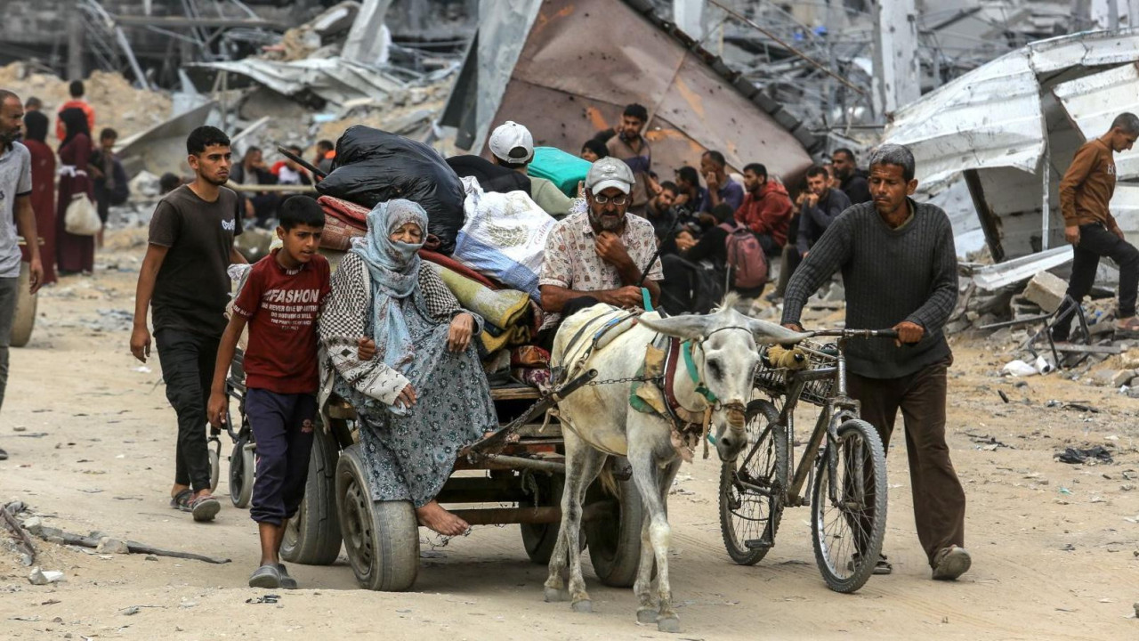 ljudi hodaju prašnjavim putem dok su iza njih razrušene zgrade 