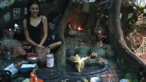 Nina Kutina u pećini blizu korena drveta, okružena malim predmetima i nakitom