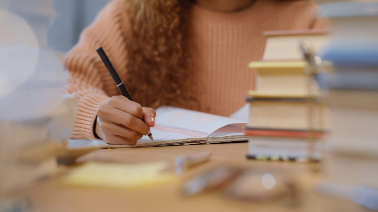 Devojčica, okružena knjigama, drži hemijsku, a pred njom je i sveska