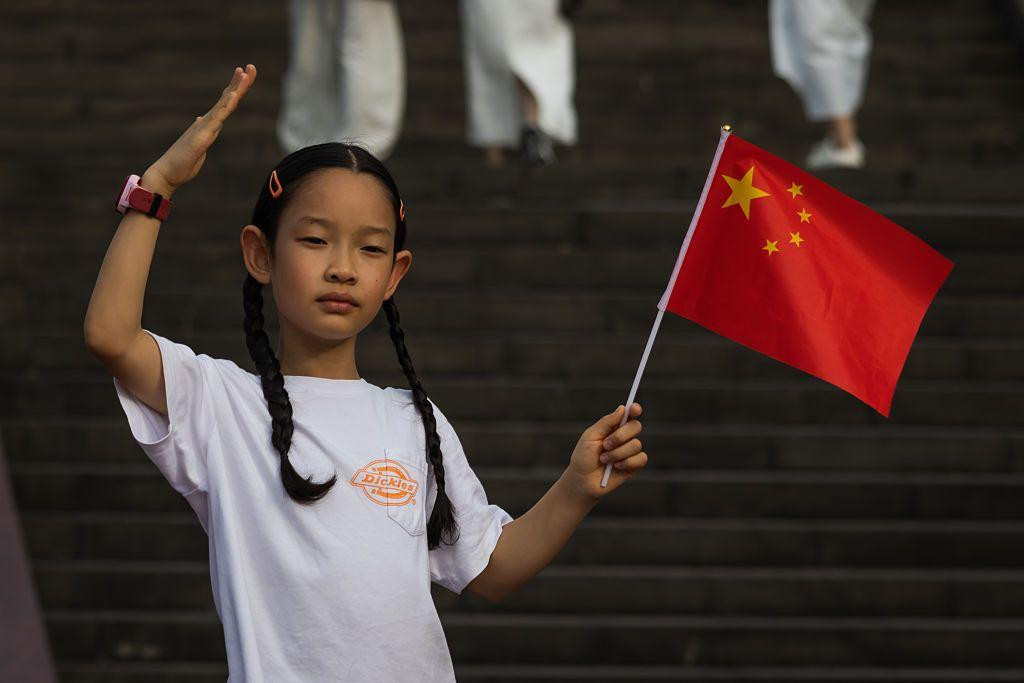 
                    A girl waves a Chinese national flag and raises her hand in salute while standing on the steps near the Chongqing People's Auditorium during the National Day Golden Week 