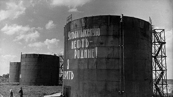 Crno-bela fotografija prikazuje dvoje ljudi koji čitaju slogan 'Nafta za otadžbinu' na velikim rezervoarima nafte u Sibiru u avgustu 1965.