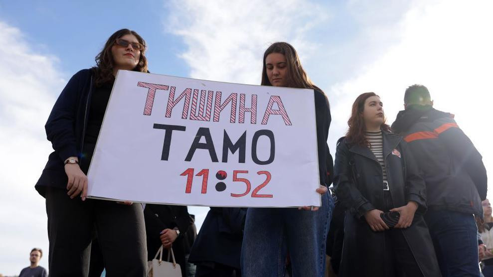 dve devojke drže transparent "Tišina tamo 11:52"