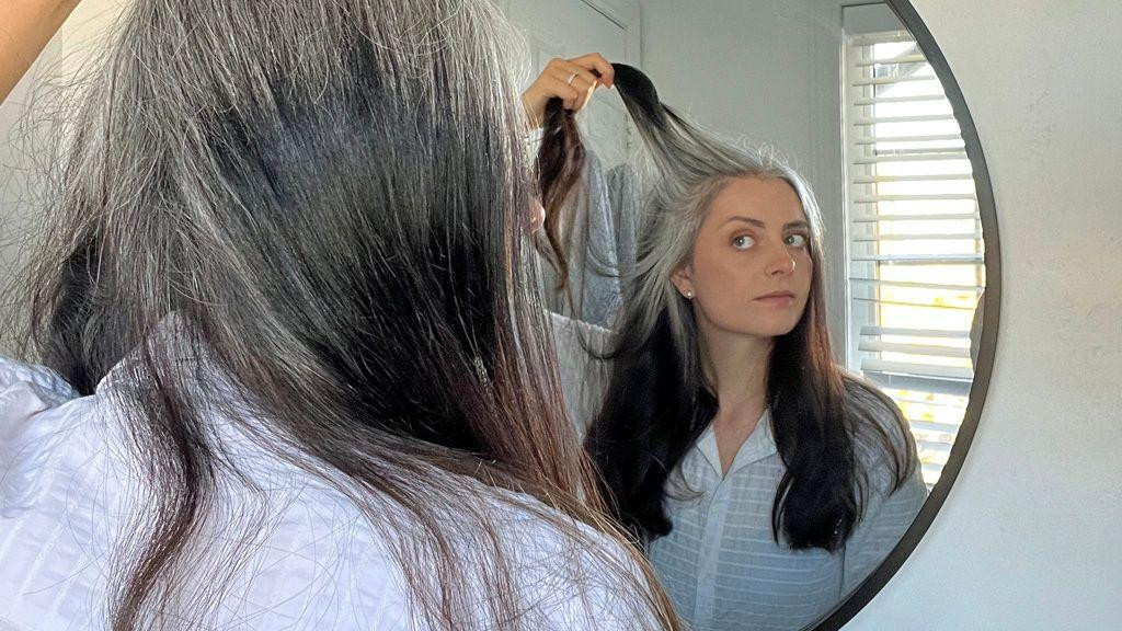 Ešli se gleda u ogledalu i drži pramen kose u ruci, a vlasi bliže korenu su sede, dok je ostatak kose taman