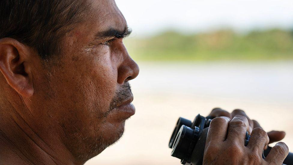 muškarac drži crni dvogled u blizini reke 