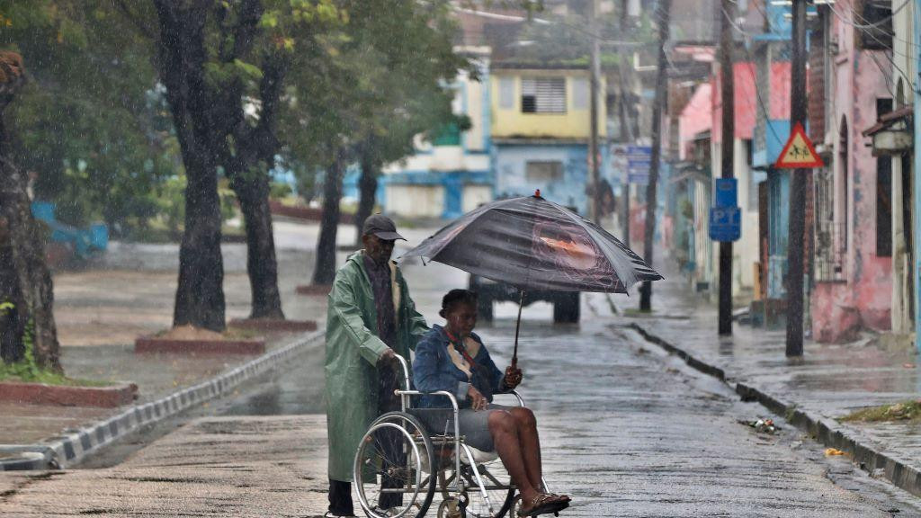Čovek guran invalidska kolica u kojima je žena koja nosi kišobran