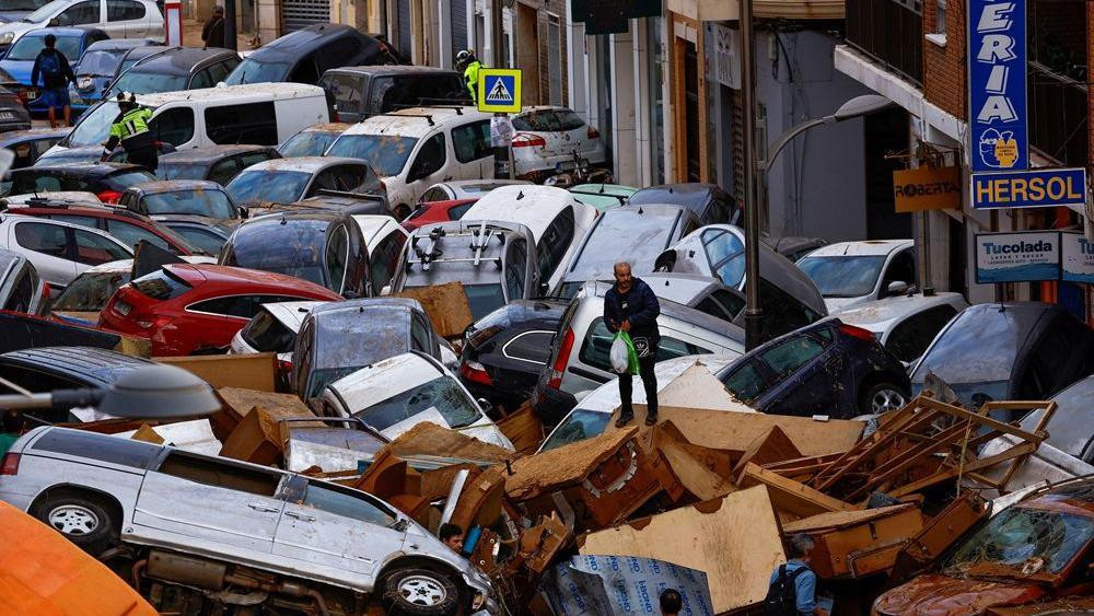 poplave u valensiji 2024, čovek stoji na nagomilanim automobilima koje je nosila bujica