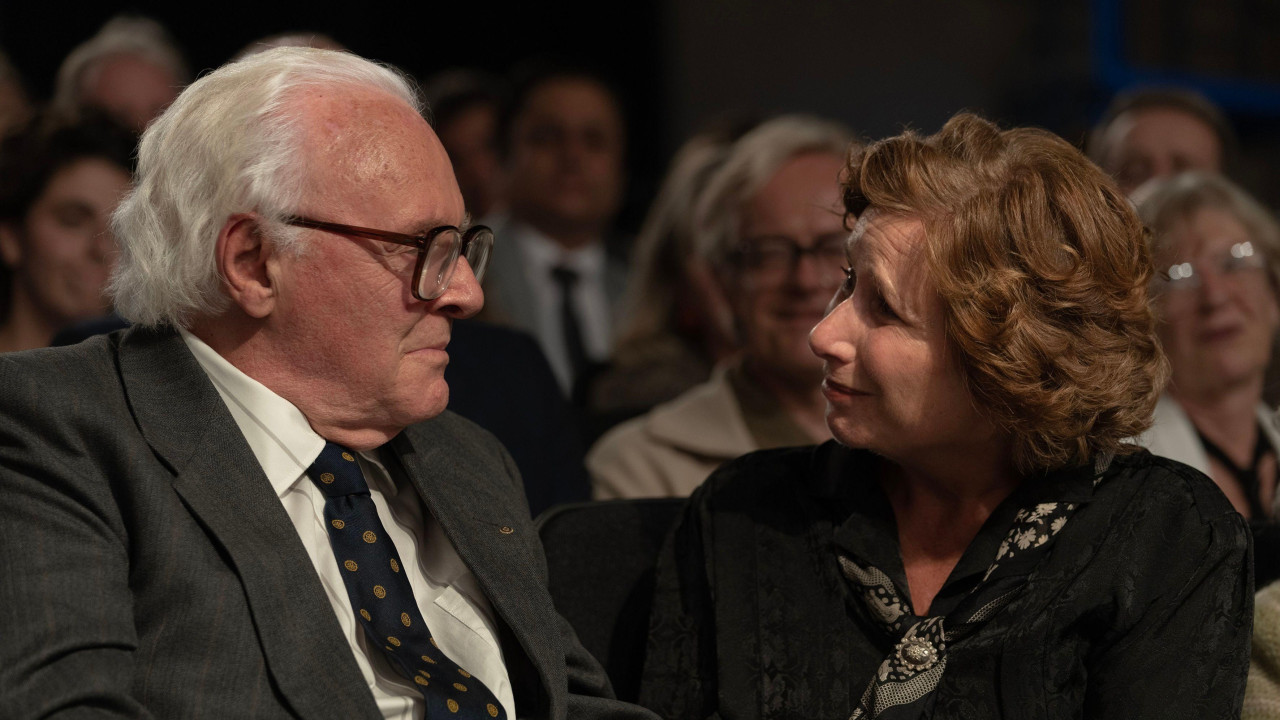 Scena iz filma Jedan život gde je Hopkins ser Nikolas Vinton u sivom odelu pored kog sedi žena u crnoj haljini sa maramom oko vrata