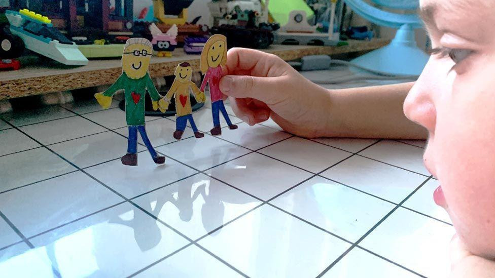 ilustracija - dete drži od kartona napravljenu porodicu