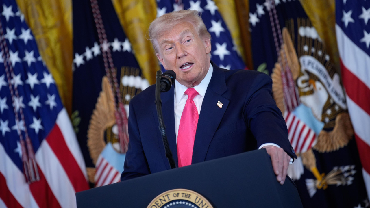 Donald Tramp daje izjavu za medije u plavom odelu i beloj košulji, sa roze kravatom, iza njega su zastave SAD